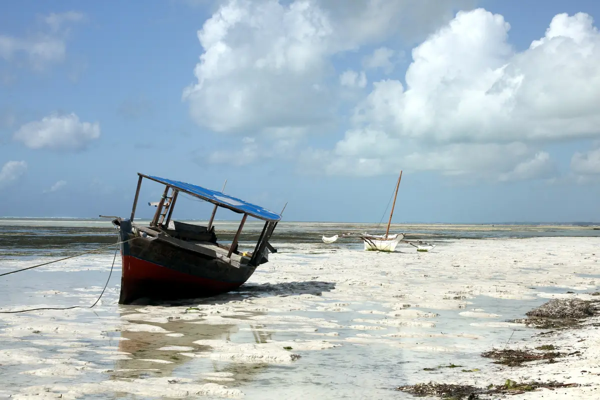 Wooden boat resting on the sand at low tide under tall clouds