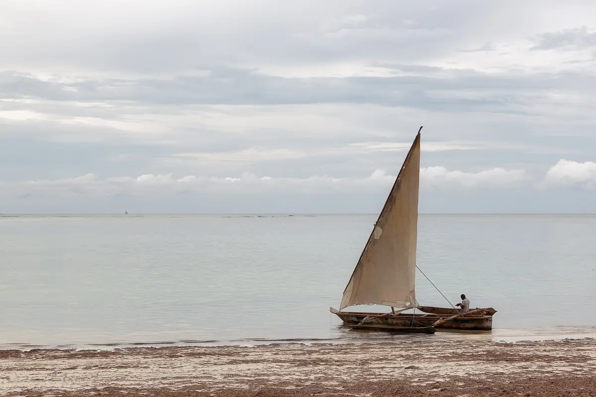 Traditional dhow with a tan sail gliding across a calm grey sea