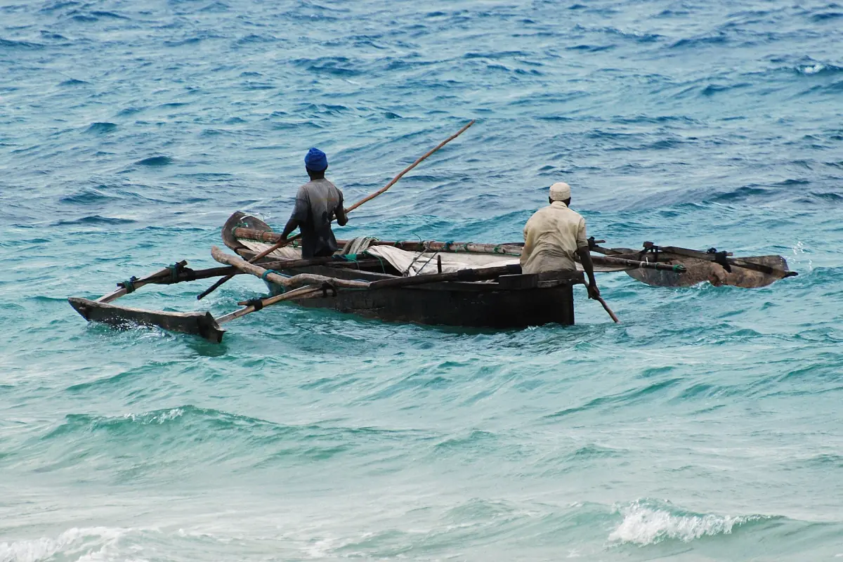 Deux hommes pagayant sur une pirogue à balancier en bois dans les vagues turquoise