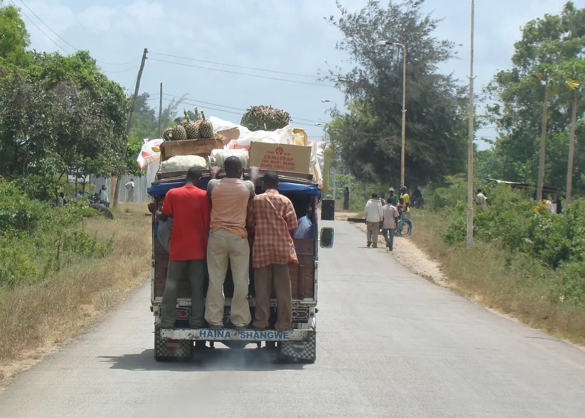 Passengers standing on the back of a dala-dala truck on a tarred road